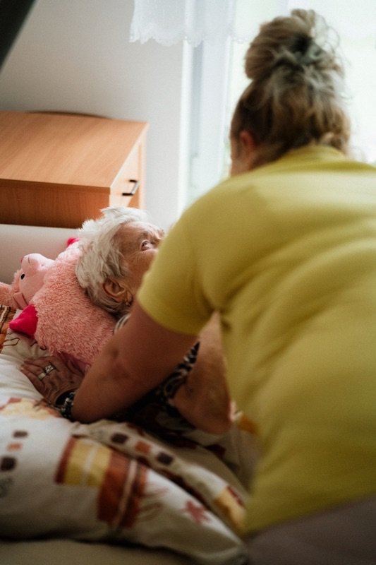 A carer leaning over an older woman resting in bed
