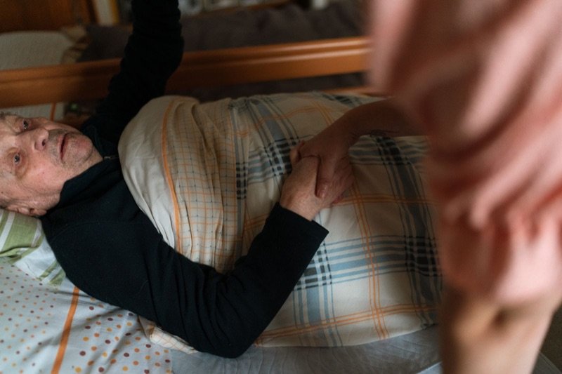 A carer holding the hand of an older person lying in bed