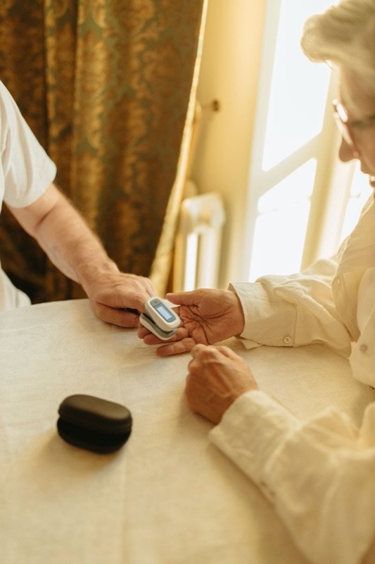 A pulse oximeter being placed on an older person's finger at home